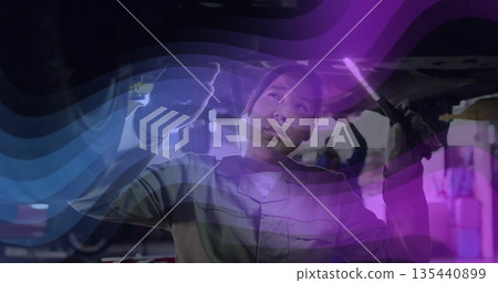 Shining torch and tightening undercarriage using wrench in repair bay female mechanic in coveralls 135440899