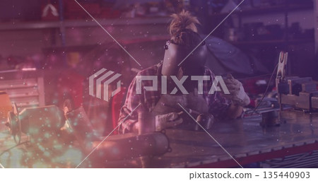 Welding metalworker wearing helmet and gloves using torch on metal piece at workshop, with sparks Welding metalworker wearing helmet and gloves using torch on metal piece at workshop, with sparks 135440903
