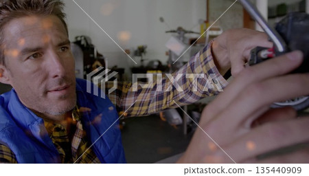 Mechanic wearing blue vest adjusting motorcycle handlebar in workshop, with tool cabinets 135440909