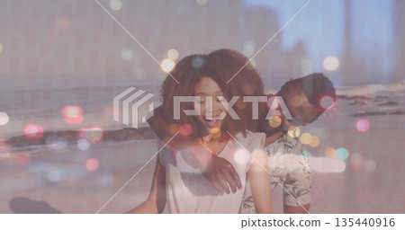 Laughing couple wearing casual beachwear standing on sandy shore, with ocean waves and pastel bokeh 135440916