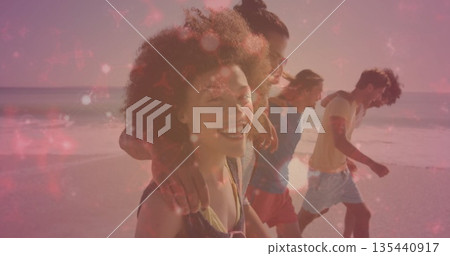 Walking four friends in beachwear draping arms over shoulders along sandy beach with sunset glow 135440917