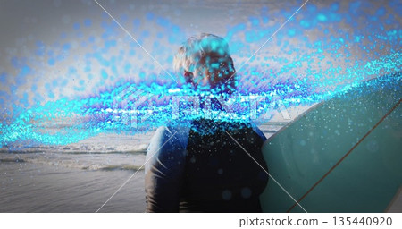 Standing senior surfer holding surfboard at beach in full-body wetsuit, with digital wave effect 135440920