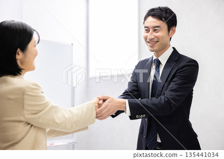 Smiling male and female business people shaking hands Smiling male and female business people shaking hands 135441034