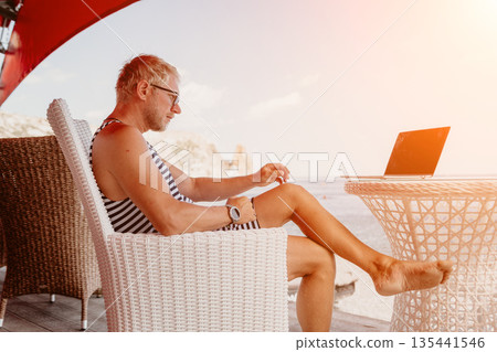 Man laptop beach working as a digital nomad on a sunny terrace overlooking the ocean during vacation Man laptop beach working as a digital nomad on a sunny terrace overlooking the ocean during vacation 135441546