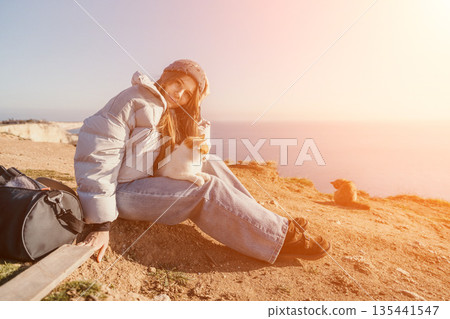 Woman cat coastal scene where a young traveler sits on a cliff with her pet during a peaceful sunset by the sea 135441547