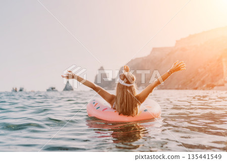 Woman, Ocean, Relaxation. Young woman on inflatable ring floats in sea with arms outstretched, enjoying summer vacation with copy space. Woman, Ocean, Relaxation. Young woman on inflatable ring floats in sea with arms outstretched, enjoying summer vacation with copy space. 135441549