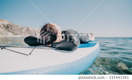 Man Relaxing Paddleboard Ocean - Man lays down on a paddleboard in the ocean and relaxes. 135441561