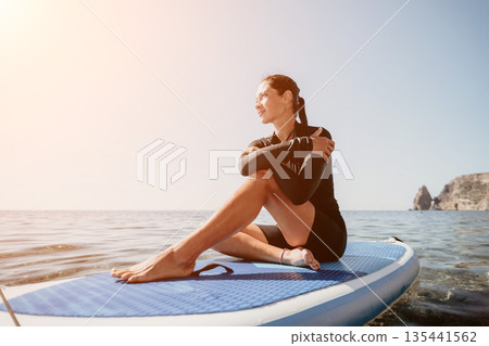 Woman Paddleboard Ocean Relaxing - Female sits on a paddleboard in the ocean, enjoying the sun and the view. Woman Paddleboard Ocean Relaxing - Female sits on a paddleboard in the ocean, enjoying the sun and the view. 135441562