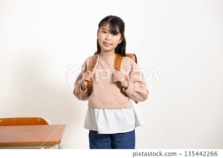 A smiling elementary school girl carrying a school bag in a classroom 135442266