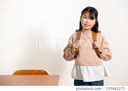 教室裡，一個帶著微笑的小學生女孩背著書包。 135442271
