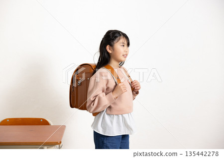 A smiling elementary school girl carrying a school bag in a classroom 135442278
