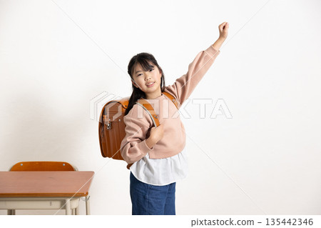 一個背著書包、微笑的小學生在教室裡揮舞著拳頭。 135442346