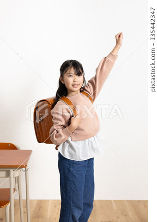 一個背著書包、微笑的小學生在教室裡揮舞著拳頭。 135442347