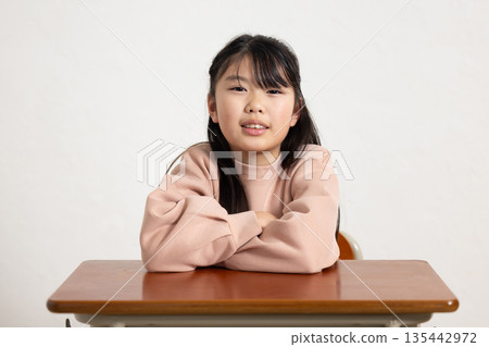 Elementary school girl smiling at the camera with her arms crossed on the desk Elementary school girl smiling at the camera with her arms crossed on the desk 135442972