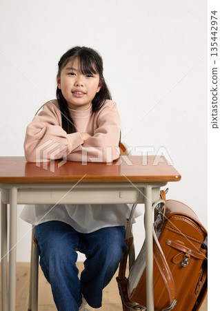 Elementary school girl smiling at the camera with her arms crossed on the desk Elementary school girl smiling at the camera with her arms crossed on the desk 135442974