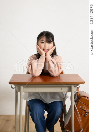 一名小學生對著鏡頭微笑,手托著下巴,手放在桌上。 一名小學生對著鏡頭微笑,手托著下巴,手放在桌上。 135442976