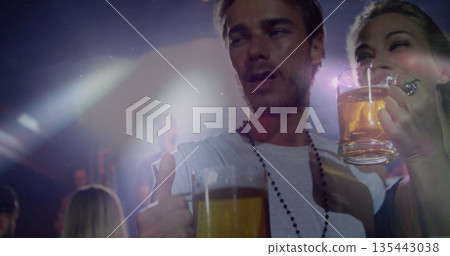 Man wearing white tee, necklace raising beer mug showing thumbs-up in bar with colored stage lights Man wearing white tee, necklace raising beer mug showing thumbs-up in bar with colored stage lights 135443038