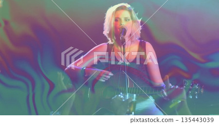 Strumming teen musician singing on stage, with acoustic guitar, microphone stand and stage lights 135443039