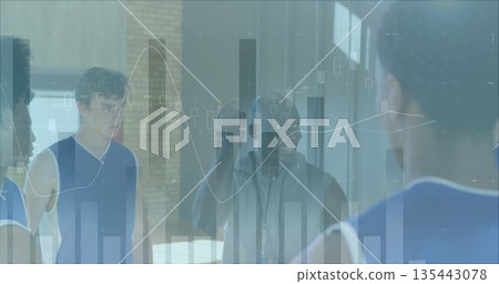Holding basketball coach speaking to players in blue jerseys on gym court, with data charts overlay Holding basketball coach speaking to players in blue jerseys on gym court, with data charts overlay 135443078