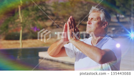 Meditating mature man praying on sunlit wooden deck beside pool, lens flare effect, copy space 135443088
