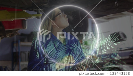 Scanning car under hoist, blue-coverall mechanic with glowing palm leaf AR overlay in shop 135443138