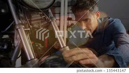 Kneeling mechanic adjusting motorcycle forks in workshop with wrench, extinguisher, copy space 135443147