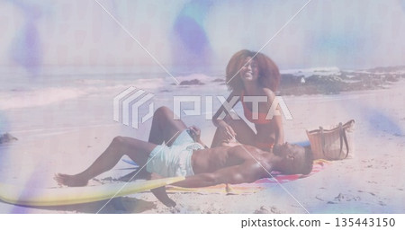Relaxing couple wearing red bikini and trunks on shore, with surfboard, beach towel and tote bag 135443150