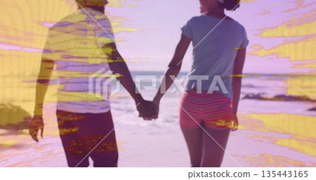 Walking couple wearing shorts and T-shirts holding hands at beach shoreline, with sand and waves Walking couple wearing shorts and T-shirts holding hands at beach shoreline, with sand and waves 135443165