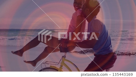 Pedaling romantic couple riding yellow bicycle along wet sandy shore, with ocean waves rolling Pedaling romantic couple riding yellow bicycle along wet sandy shore, with ocean waves rolling 135443169
