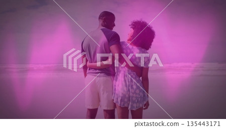 Standing couple embracing waists facing ocean horizon at seaside beach, with pink heart overlays Standing couple embracing waists facing ocean horizon at seaside beach, with pink heart overlays 135443171