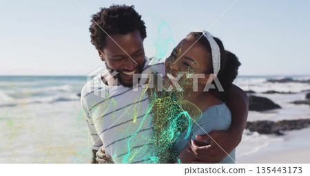 Smiling couple wearing off-shoulder top and white t-shirt embracing on beach with white headband Smiling couple wearing off-shoulder top and white t-shirt embracing on beach with white headband 135443173