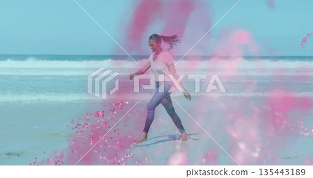 Walking barefoot woman in white tee and jeans along shallow shoreline, with pink powder splashes Walking barefoot woman in white tee and jeans along shallow shoreline, with pink powder splashes 135443189