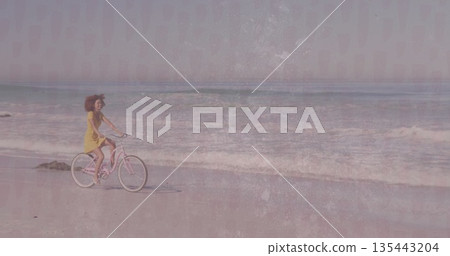 Pedaling woman wearing yellow dress on pastel pink cruiser bicycle along sand at beach, copy space Pedaling woman wearing yellow dress on pastel pink cruiser bicycle along sand at beach, copy space 135443204