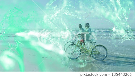 Standing man and woman facing sea on beach, with cruiser bicycles and green digital network overlay Standing man and woman facing sea on beach, with cruiser bicycles and green digital network overlay 135443205