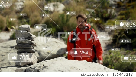 Standing male hiker wearing red jacket on rocky riverbed, with stone cairn and notification icons 135443218
