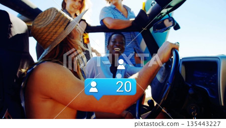 Group of four friends cruising in open-top off-road vehicle along coastal highway, with straw hat 135443227