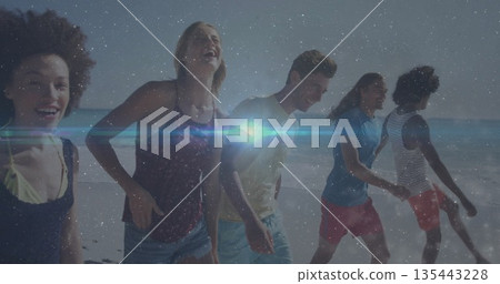 Strolling five friends laughing, smiling at sandy shore edge, with lens flare and starry overlay 135443228