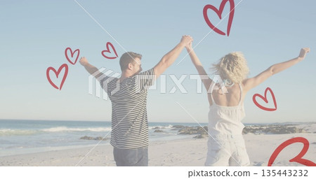 Raising arms and holding hands couple wearing beachwear on beach, ocean waves, red heart doodles Raising arms and holding hands couple wearing beachwear on beach, ocean waves, red heart doodles 135443232