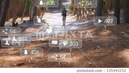 Walking mature photographer raising camera on forest trail, with floating social media icons Walking mature photographer raising camera on forest trail, with floating social media icons 135443252
