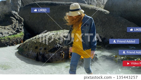 Walking woman navigating rocky tidal pool, with straw sun hat, denim jacket  and  floating social ic 135443257