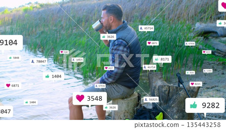 Man in vest sipping from camping mug on lakeside stump, fishing rod, social icons, copy space 135443258