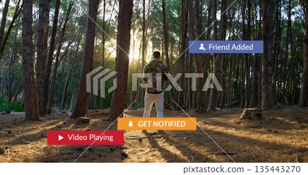 Viewing notification overlays, man in camouflage shirt holding smartphone at pine forest clearing 135443270