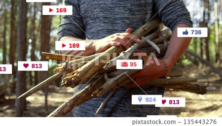 Man exploring forest clearing, holding bundle of dry branches, with digital overlay icons Man exploring forest clearing, holding bundle of dry branches, with digital overlay icons 135443276