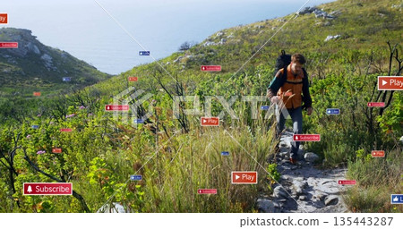 Mid male hiker traversing narrow coastal trail with backpack, stick and floating icons, copy space 135443287