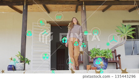 Standing woman scanning floating eco and energy icons on front terrace, ceramic pots and columns Standing woman scanning floating eco and energy icons on front terrace, ceramic pots and columns 135443296