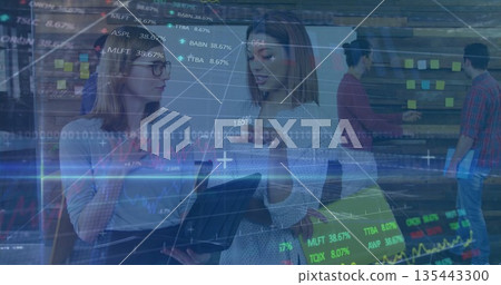 Collaborating businesswomen pointing at laptop in office, with sticky notes and market charts 135443300