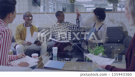 High-fiving professionals in mustard jacket and overalls in office lounge, with printed documents High-fiving professionals in mustard jacket and overalls in office lounge, with printed documents 135443360