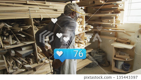 Senior woodworker wearing apron inspecting lumber at woodshop, with social media overlay 135443397