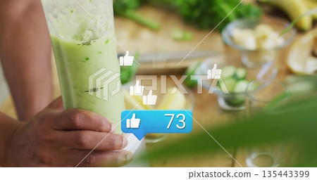Cook holding blender jar pouring smoothie in kitchen, with produce, knife, social icons, copy space 135443399