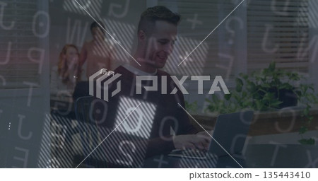 Man typing on laptop at office desk near observing colleagues, with striped blinds, potted plant 135443410